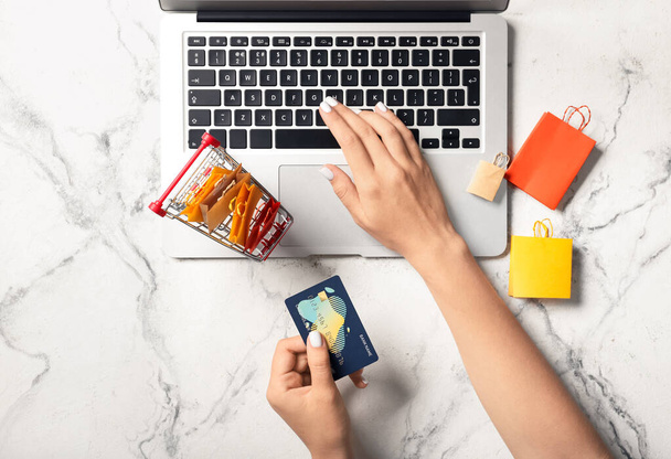 Mulher usando laptop e segurando cartão de crédito no fundo claro, close-up - Foto, Imagem