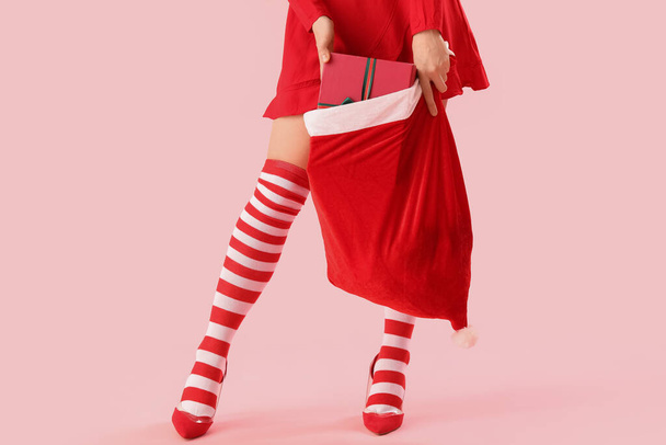 Νεαρή γυναίκα σε χριστουγεννιάτικες κάλτσες με τσάντα σε ροζ φόντο - Φωτογραφία, εικόνα