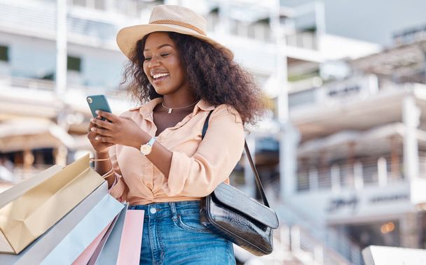 Shopping bag, smartphone and black woman in city with retail sale announcement, newsletter discount code or ecommerce website. Wealth, success customer in urban outdoor using phone for online choice. - Foto, Imagen