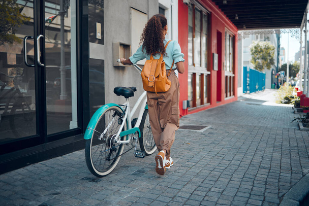 Bike, city and back view of black woman, walking on street or urban road outdoors. Exercise, fitness and female student on bicycle ride, eco friendly transportation and cycling on asphalt in town - Foto, afbeelding