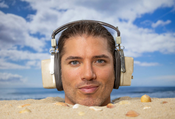 Egy férfi a tengerparton a fejéig eltemetve zenét hallgatott fejhallgatón. - Fotó, kép