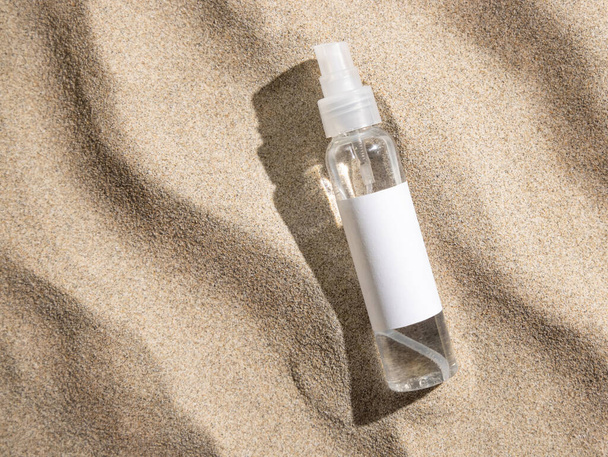 Spray bottle with blank label on beige sand top view, hard light. Package mockup. Natural skincare or SPA product. Facial cosmetics for beauty routine. Zen style with waves on sand, minimal aesthetic - Photo, Image