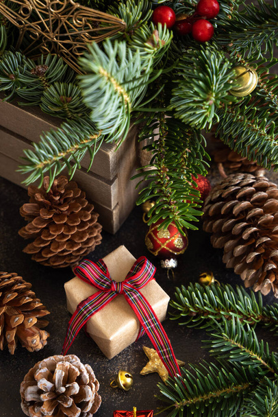 Wrapped gift boxes between Christmas decorations, pine cones and green fir branches close up. Christmas or New Year Holiday atmosphere flat lay - 写真・画像
