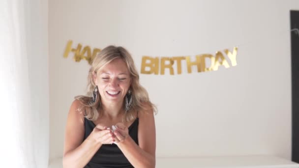 A beautiful woman celebrates her birthday. BLONDE woman blows bright glitter in front of her face. Slow motion - Footage, Video