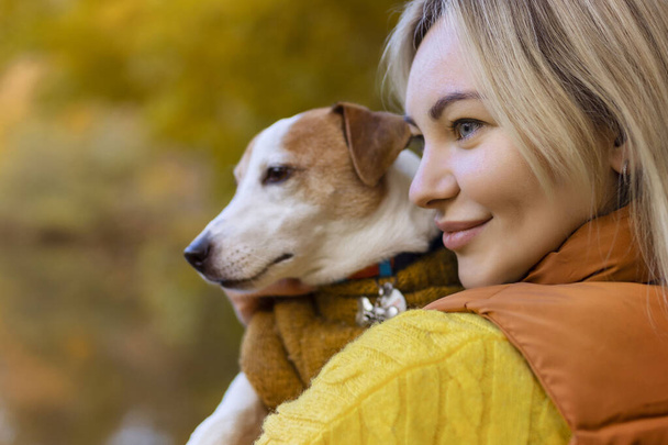 Portrait of a smiling young woman kissing a dog in a field. Dog lover stylish girl hugging her dog while walking. Animal friendship concept.  - Foto, immagini