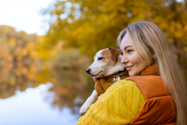 Портрет улыбающейся молодой женщины, целующей собаку в поле. Любитель собак стильная девушка обнимает свою собаку во время прогулки. Концепция дружбы животных.  - Фото, изображение