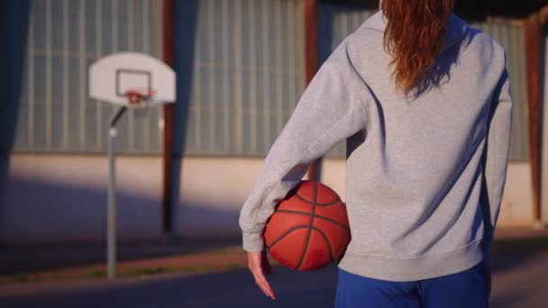 Retrato de uma menina com um basquete em um campo de basquete esportivo ao pôr do sol. Imagens 4k de alta qualidade - Filmagem, Vídeo