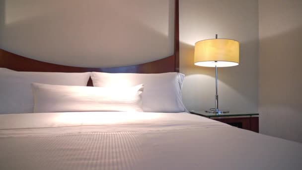 Белые подушки и одеяло на кровати украшают интерьер спальни отеля  - Кадры, видео