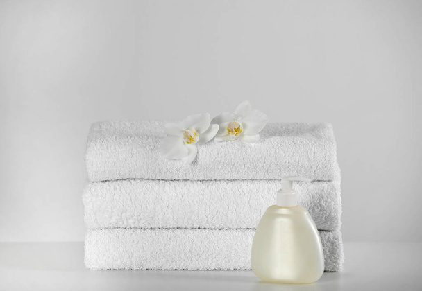 Soft folded towels, orchid flowers and dispenser on white table - Foto, imagen