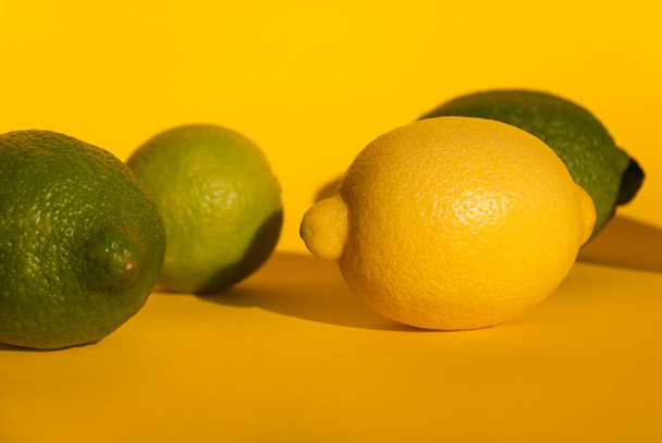 Yellow and green lemons fruit on yellow background with hard shadows. Citrus fruits - Zdjęcie, obraz