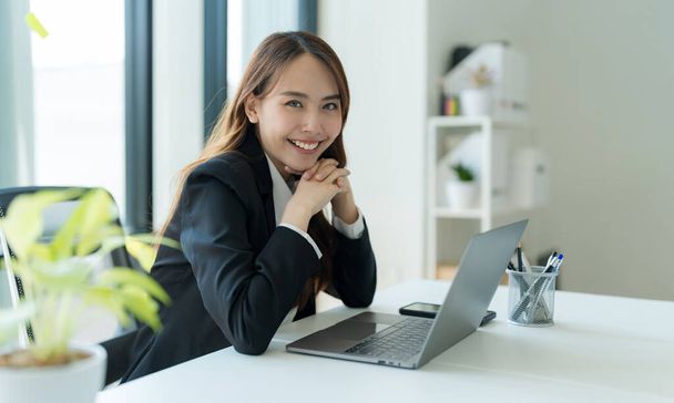 Aufnahme einer glücklichen jungen asiatischen Frau, die in die Kamera schaut, Attraktive Geschäftsfrau, die in ihrem Büro am Laptop arbeitet. - Foto, Bild
