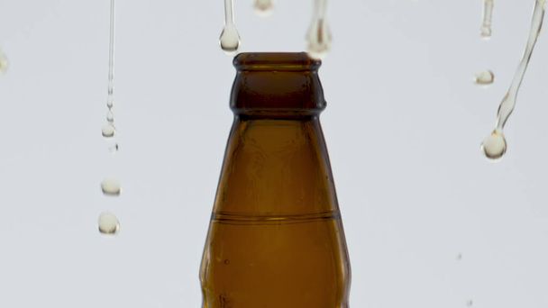 Craft gouden bier spatten uit de fles na opening in super slow motion close-up. Gele druppels exploderen op witte achtergrond. Tarwemout alcoholische drank voor een verfrissend feest. - Foto, afbeelding