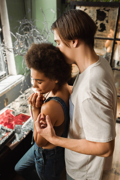 high angle view of man hugging young and pretty african american girlfriend in workshop - Foto, imagen