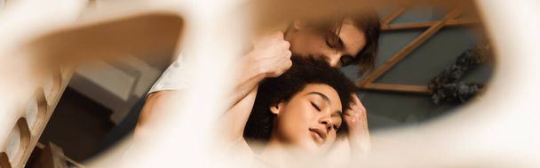 nízký úhel pohledu na vášnivý mezirasový pár se zavřenýma očima držící se za ruce na rozmazaném popředí, banner - Fotografie, Obrázek