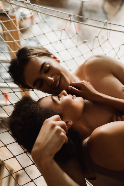 shirtless man and pretty african american woman smiling at each other in hammock  - Фото, зображення