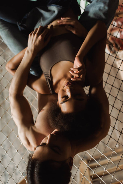 vista superior del hombre joven sin camisa abrazando a la mujer afroamericana en la parte superior de la hamaca de malla en el estudio de arte - Foto, Imagen
