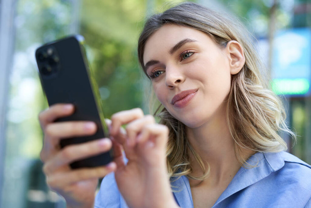女性社員が屋外に座って携帯電話を見て、スマートフォンの画面で笑顔. - 写真・画像