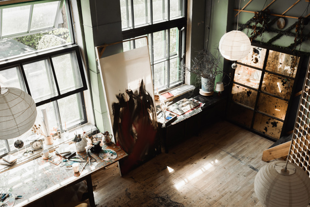 Blick in die geräumige Werkstatt mit großen Fenstern und Kunstwerkzeugen auf Fensterbänken unter Kugelleuchtern  - Foto, Bild
