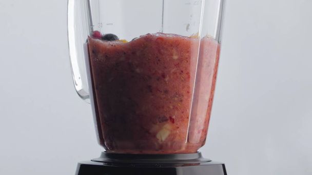 Elektrische shaker mengen van natuurlijke sappige fruit smoothie in super slow motion close-up. Biologische gesneden bosbessen sinaasappel aardbei mengen in glazen blender kom bereiden paarse mix. Vegetarische voeding - Foto, afbeelding
