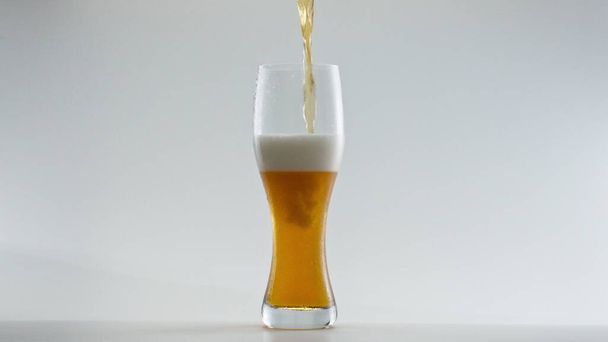 Fresh tasty lager beer filling clear glass in super slow motion close up. Stream of wheat alcohol drink pouring into transparent goblet at white background. Hop liquid bubbling foaming in mug. - Photo, Image