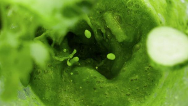 Fresh vegetables falling in green vitamin smoothie preparing with electric blender close up. Tasty raw broccoli cucumber spinach kale adding in mixer bowl super slow motion. Top view blending puree. - Photo, Image