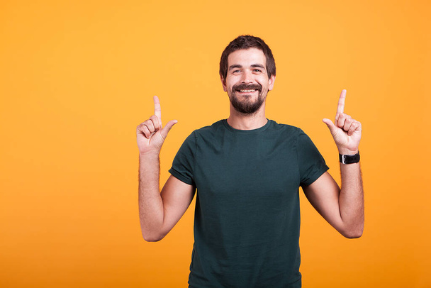 Happy man smiling and pointing up with his fingers. Copyspace available for your text and advertisement promotion. Shot on orange background - Photo, Image