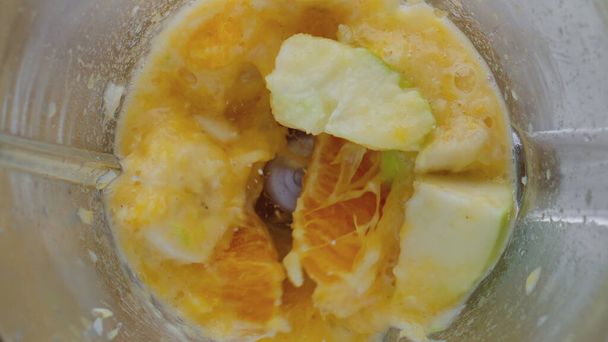 Closeup het bereiden van zoete smakelijke vruchtenpuree van appel banaan mandarijn in elektrische blender. Snijd sappige ingrediënten mengen in mixer kom in super slow motion. Gezonde vegetarische voeding. - Foto, afbeelding
