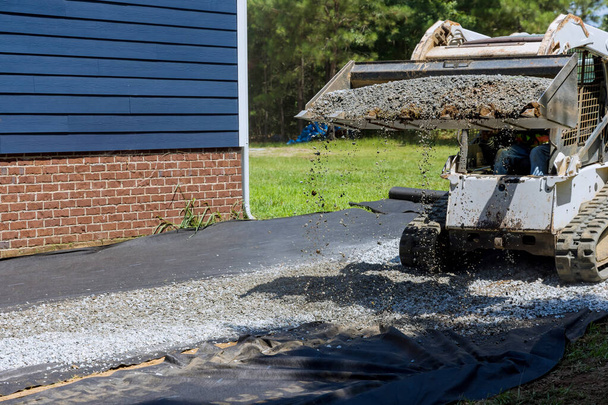 Tractor heeft geüpload grind voorbereiding platform waarop opslag schuur zal worden geïnstalleerd in de buurt van huis - Foto, afbeelding