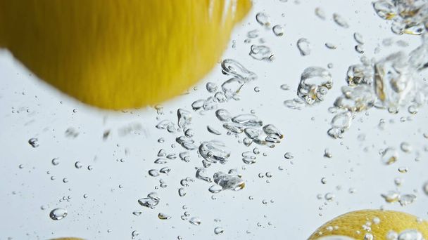 Baloncuklarda düşen organik limonlar yakın plan. Çok güzel taze narenciye arkaplanda yüzen bir sıvı bırakıyor. Sağlıklı yemek için sarı ekşi meyveler. Rahatlama reklam çekimi. - Fotoğraf, Görsel