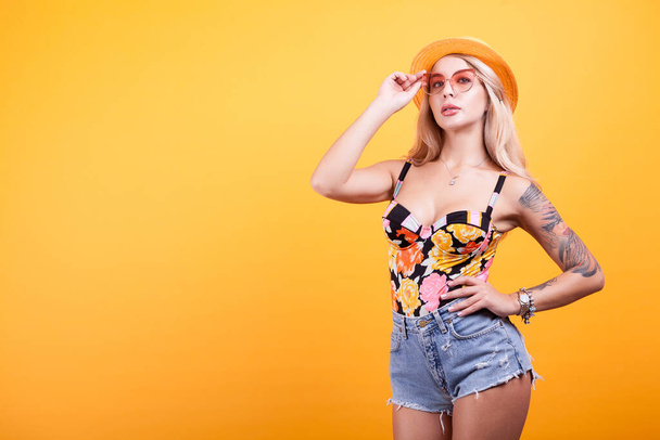 若いセクシーな黄色の背景の上のサングラスと帽子と水着で日焼けした女性をスリムします。 - 写真・画像