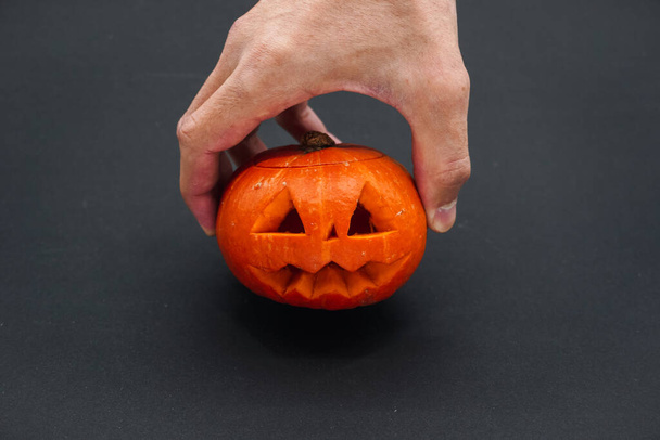 A man is holding a carved small pumpkin. Hand with pumpkin close-up on black background. - Photo, Image