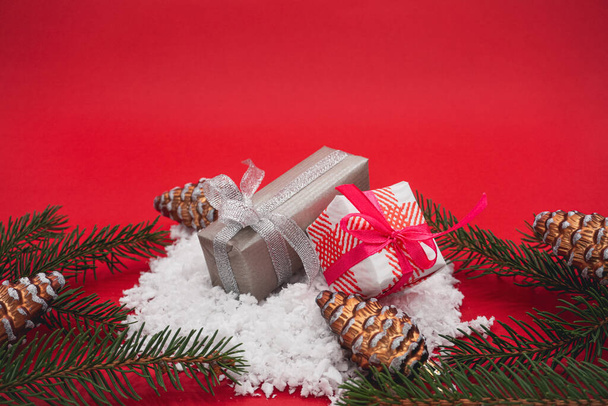 Deux cadeaux de Noël dans la neige, parmi des cônes de pin. Sur fond rouge. - Photo, image