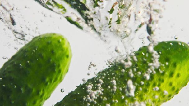 Frisches Gemüse fällt Wasser in Blasen Nahaufnahme. Frische bunte Gurken Kirschtomaten, die in transparenter Flüssigkeit planschen. Sommer-Bio-Zutaten für gesunden Salat. Fitness-Kochgenuss. - Foto, Bild