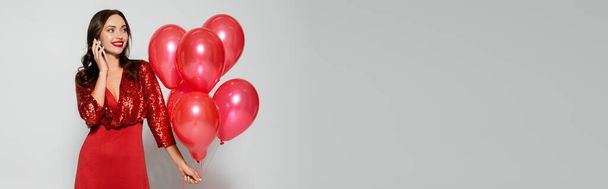 Pretty woman in red dress holding balloons and talking on smartphone on grey background, banner  - Foto, Imagem