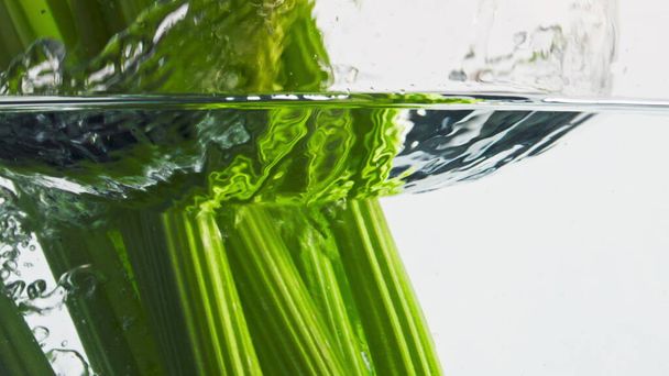 セロリの茎は水の表面を閉じます。健康的な有機食品の商業。新鮮な緑の植物は、光の背景に透明な液体に落ちます。フィットネス低カロリー成分。ベジタリアン食のコンセプト - 写真・画像