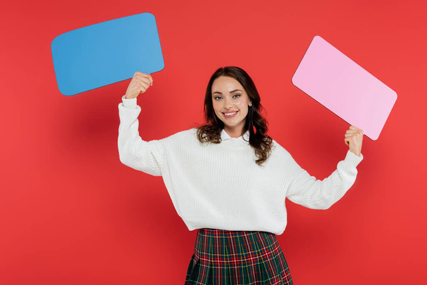 Cheerful woman in cozy sweater holding speech bubbles on red background  - Fotó, kép