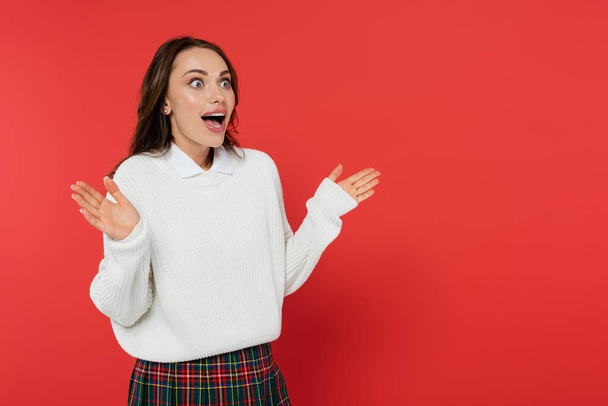 Shocked woman in warm sweater looking away isolated on red  - Foto, imagen
