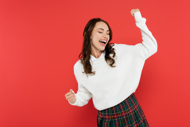 Happy young woman in sweater dancing isolated on red  - Foto, imagen