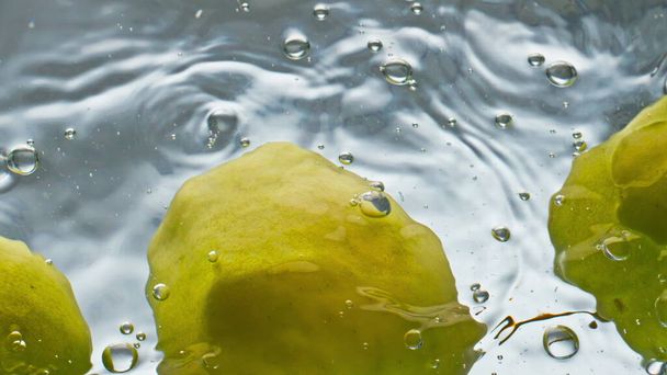Органические яблоки, плавающие вблизи поверхности воды. Вкусные зеленые фрукты отскакивают на светлом фоне. Это реклама натуральных продуктов питания. Низкокалорийный фитнес-ингредиент. Концепция естественного отдыха. - Фото, изображение