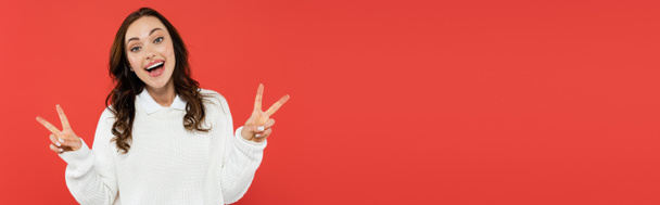 Excited woman in white jumper showing victory sign and looking at camera isolated on red, banner  - Photo, Image