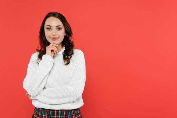 Smiling brunette woman in white jumper looking at camera isolated on red  - Fotografie, Obrázek