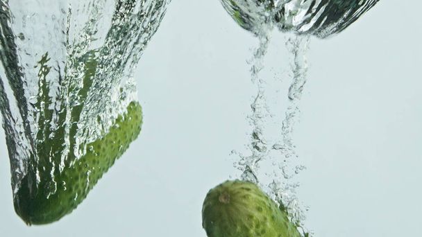 Los pepinos frescos dejan caer el agua de cerca. Bajo en calorías fitness ingrediente nutricional que cae lavado burbujeante líquido. Deliciosas verduras verdes salpican haciendo remolino en el fondo claro. Concepto de alimentación saludable - Foto, imagen