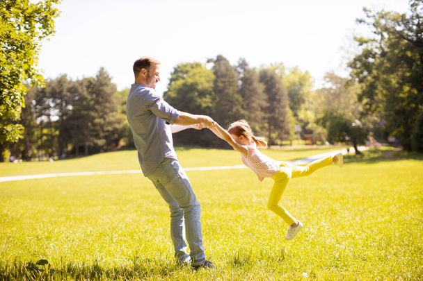 Babası ve küçük tatlı kızı parkta çimlerde eğleniyorlar. - Fotoğraf, Görsel