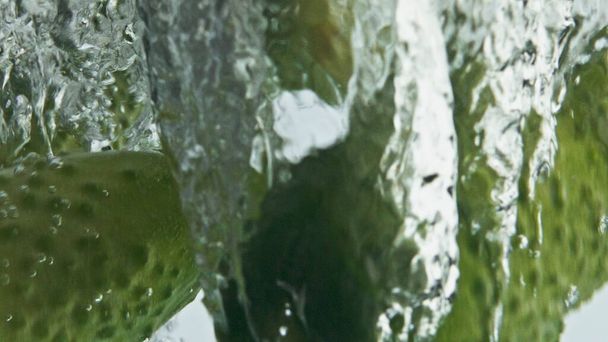 Pepinos orgánicos salpican agua en burbujas de primer plano. Hermosa toma comercial de cocina de estilo de vida saludable fitness. Verduras frescas de verano caen fluyendo en líquido transparente. Alimentación cruda baja en calorías. - Foto, imagen