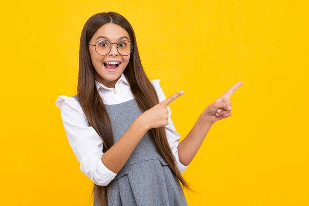 Wow, its unbelievable. Shocked teenager child pointing aside at copy space. Teen girl pointing with two hands and fingers to the side. Excited face, cheerful emotions of teenager girl - Foto, imagen