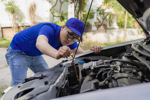 Młody mężczyzna sprawdza poziom oleju w samochodzie i naprawia wskaźnik ciśnienia w oponach przed wyjazdem.. - Zdjęcie, obraz