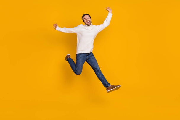 Photo of funky childish guy dressed white sweater running jumping high isolated yellow color background. - Foto, Bild