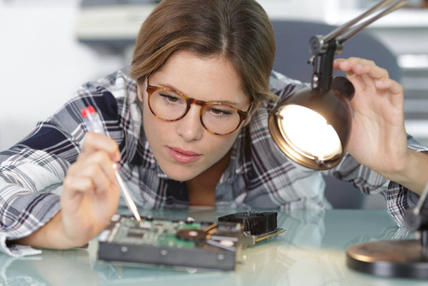 female computer technician directing lamp onto electronic component - Fotoğraf, Görsel