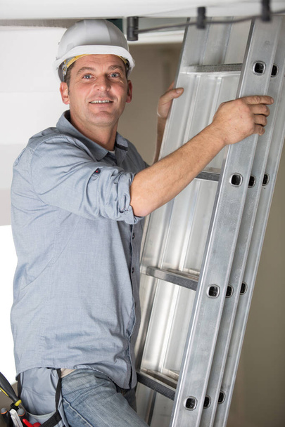 hard worker man in a ladder smiling at the camera - Foto, Imagem