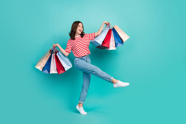 Full length photo of pretty cute lady wear striped t-shirt walking shopping looking empty space isolated turquoise color background. - Zdjęcie, obraz